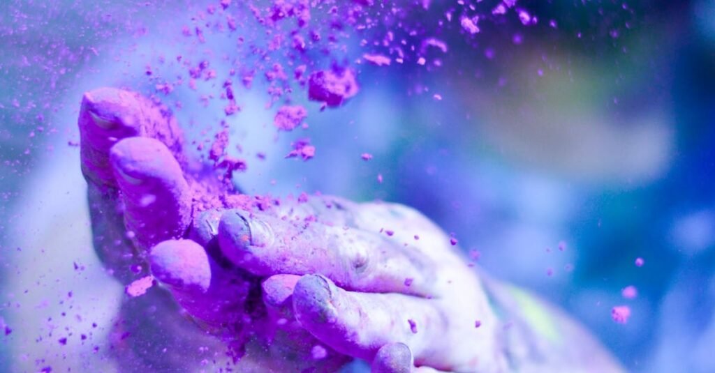 Close-up of hands throwing vibrant purple powder outdoors, capturing motion and color.